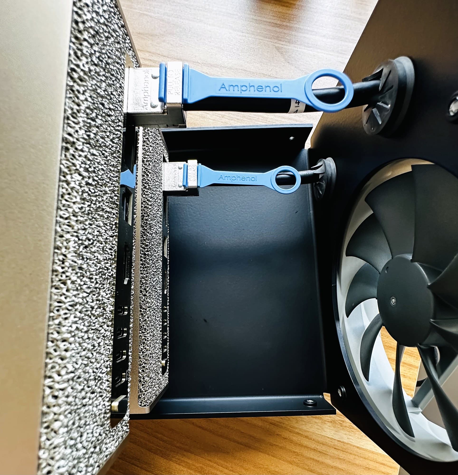 Detail of blue-tabbed Amphenol cables connected inside the Stackcooler TP2 base, next to the fan, on a wood desk.