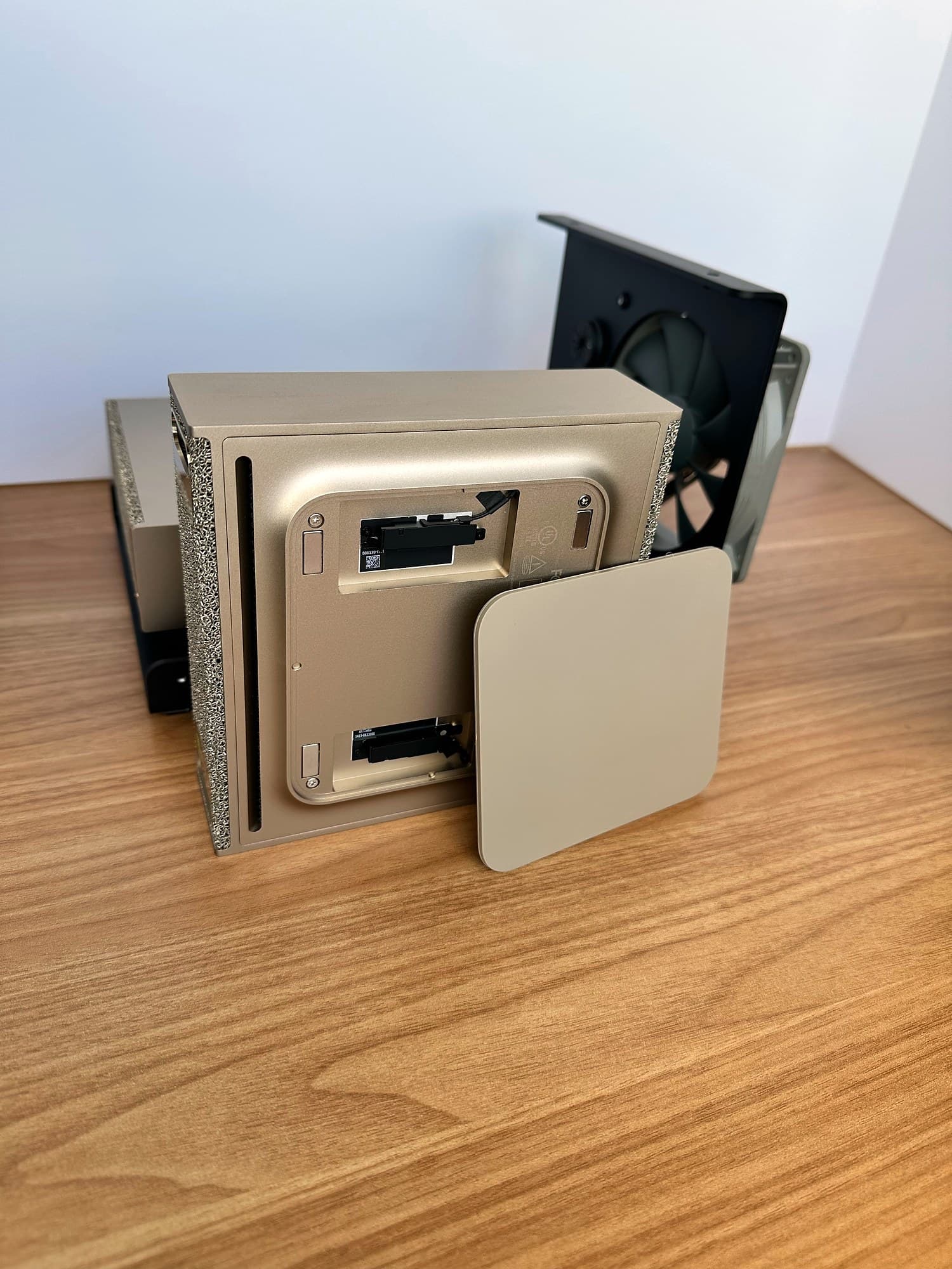 NVIDIA DGX Spark standing on its side with its gold magnetic bottom pad removed and leaning against it, on a wood desk.