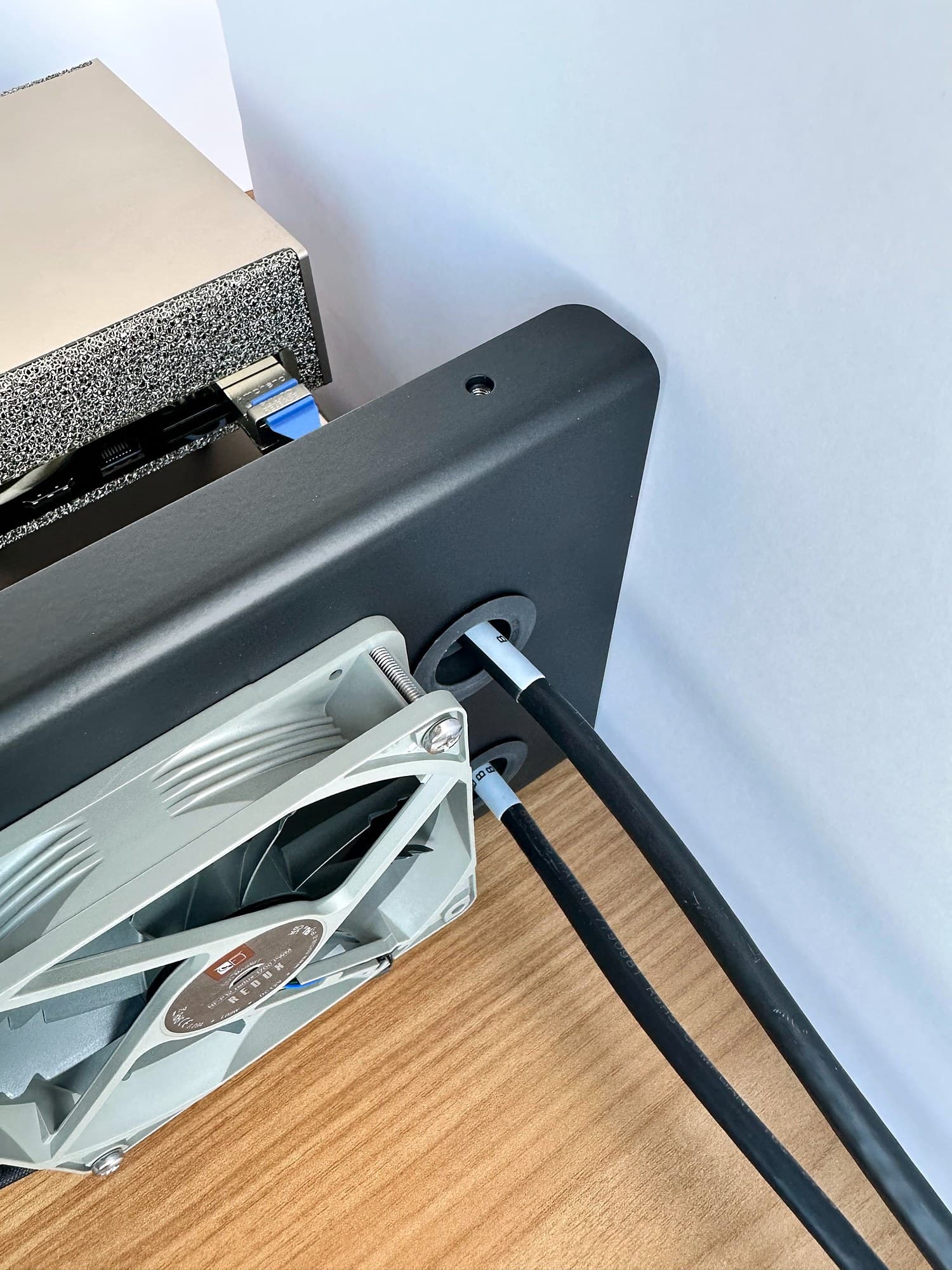 Close-up of two black cables routed through the grommeted cable entry points beside the Stackcooler TP2 rear fan.