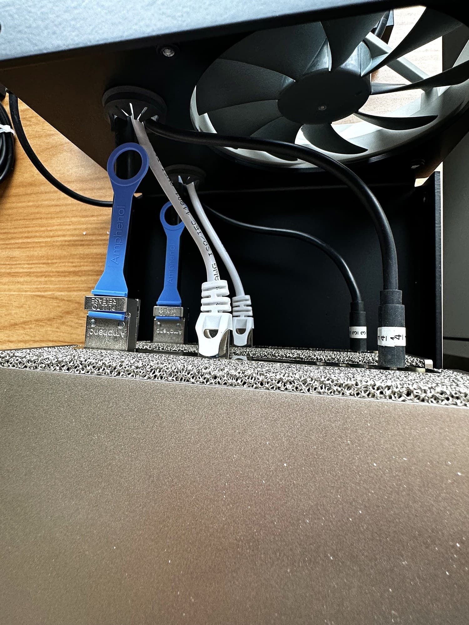 Cables routed up through the grommets under the Stackcooler: blue Amphenol QSFP pull tabs, white Ethernet and black power cables, with the fan above and the Spark below.